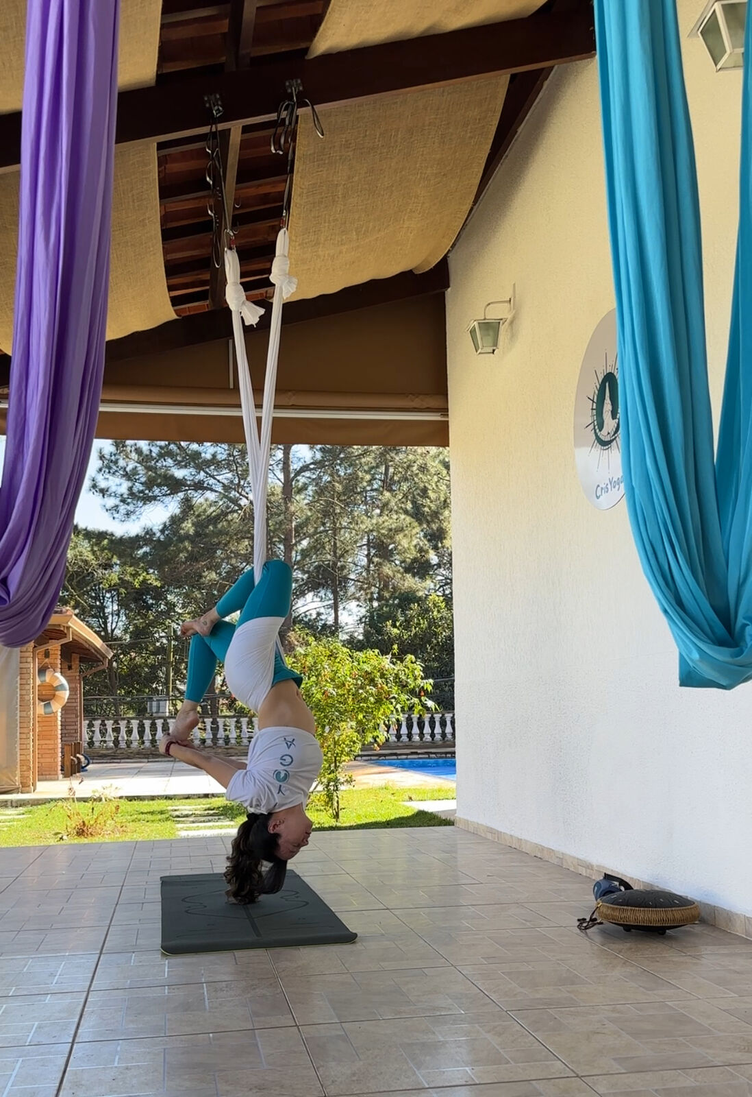 Cristina praticando Aerial Yoga no espaço coberto do studio, com vista para o jardim